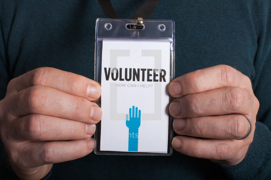 A man holding a volunteer badge with both hands.