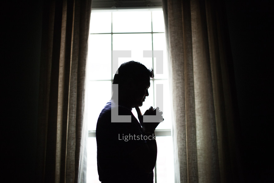 silhouette of an Indian man in prayer in front of a window 