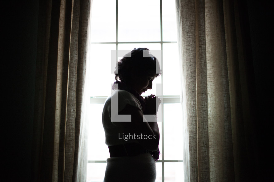 a silhouette of a woman in prayer at a window 