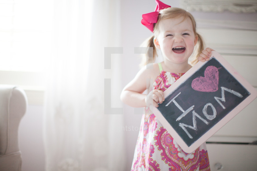 a little girl holding a chalkboard sign that reads I heart mom 