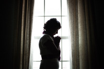 a silhouette of a woman in prayer at a window 