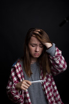 A teen girl looks at a pregnancy test with anxiety.