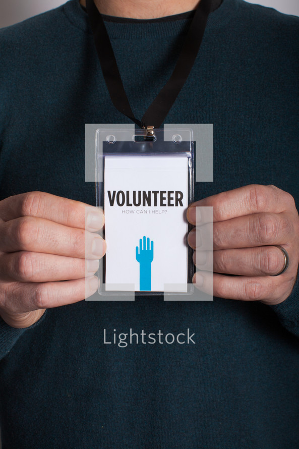 A man holding out a volunteer badge which he is wearing around his neck.