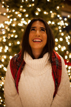 a happy woman standing in front of a Christmas tree looking up 