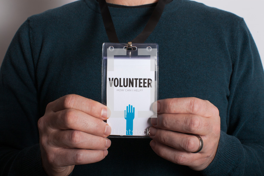 A man holding out a volunteer badge which is around his neck.