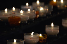 many lit candles in a dark church. 
candle, lit, flame, fire, burning, candles, flames, kindled, light, lighted, blaze, blazing, burning, burn, many, much, lot, dark, lighten, brighten, bright, illuminate, illumine, shine, shining, see, seeing, show, showing, symbol, symbolic, symbolize, symbolizing, believe, believers, wax, church, pray, prayer, votive, darkness, burnt, donation, donate, ceremony, offering, offer, yellow, white, orange, row, line, lines, commemorate, remember, recall, remembrance, memory, memento, think of, sign, creed, unlit, rows