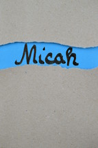 torn open kraft paper over blue paper with the name of the prophetic book Micah