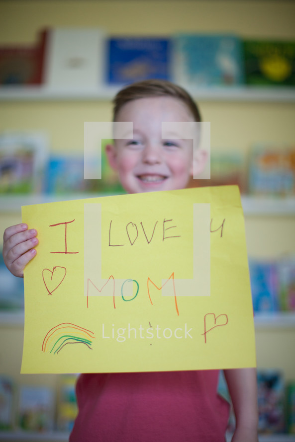 a little boy holding a sign that reads Iove mom 