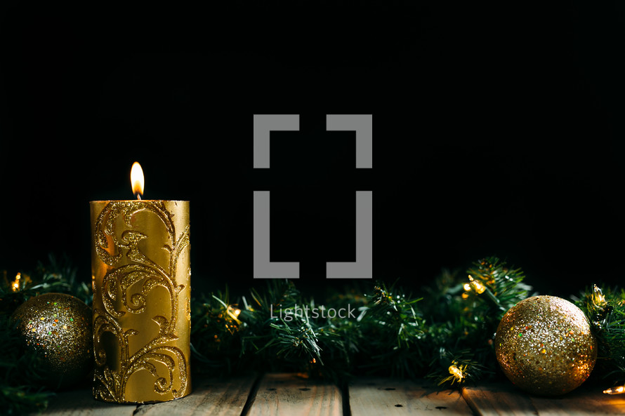 gold ornaments, pine garland, Christmas lights, and candle 