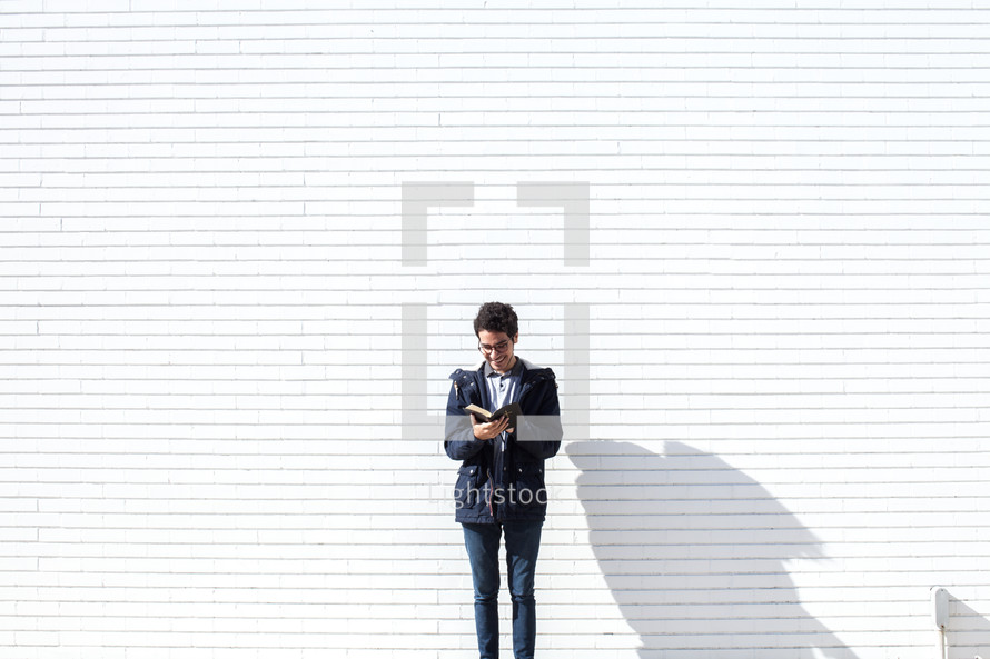 a man standing in front of a white wall reading a Bible