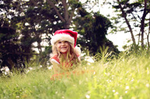 a little girl in a santa hat hiding in the grass