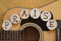 part of a guitar with the letters PRAISE burned into wooden pieces