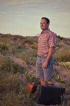 a man standing with luggage on sand dunes 