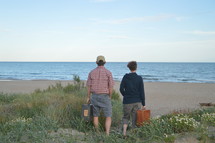 a couple with suitcases looking out at a beach 
