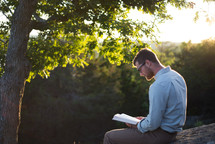 man sitting on a rock reading a Bible 