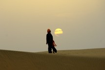man standing in front of the setting sun in the desert 