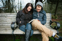 Mother and son praying together over a Bible, while sitting outside on a park bench.