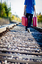 man on railroad tracks walking with luggage 