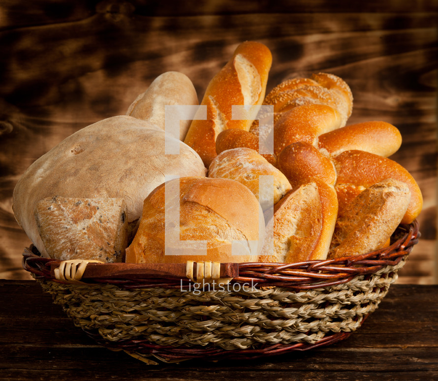 Wicker basket with different types of bread on wooden table.