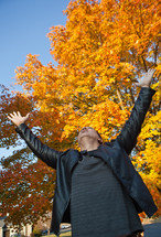 man with his hands raised in worship to God under fall leaves
