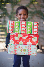 boy child holding stacked Christmas gifts 