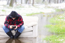 A man sits on a couch that is outside sitting in water.