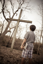 teen boy holding a Bible standing in front of a cross 