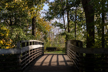 Wooden bridge and bench through green trees