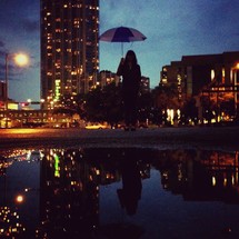A woman holding an umbrella in a city at night. 