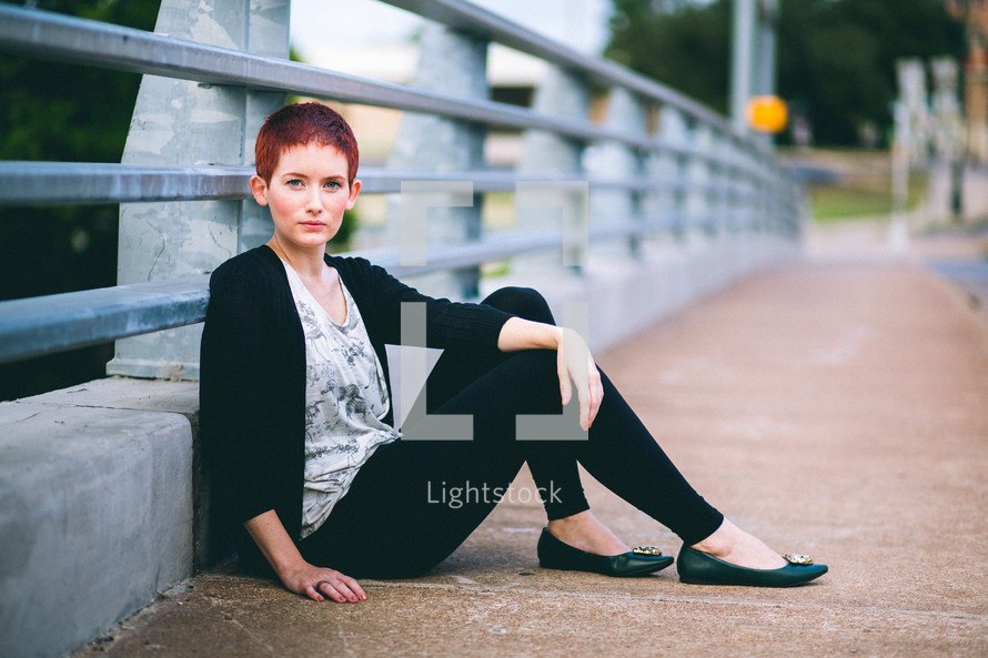 Woman sitting against the railing of an overpass. 