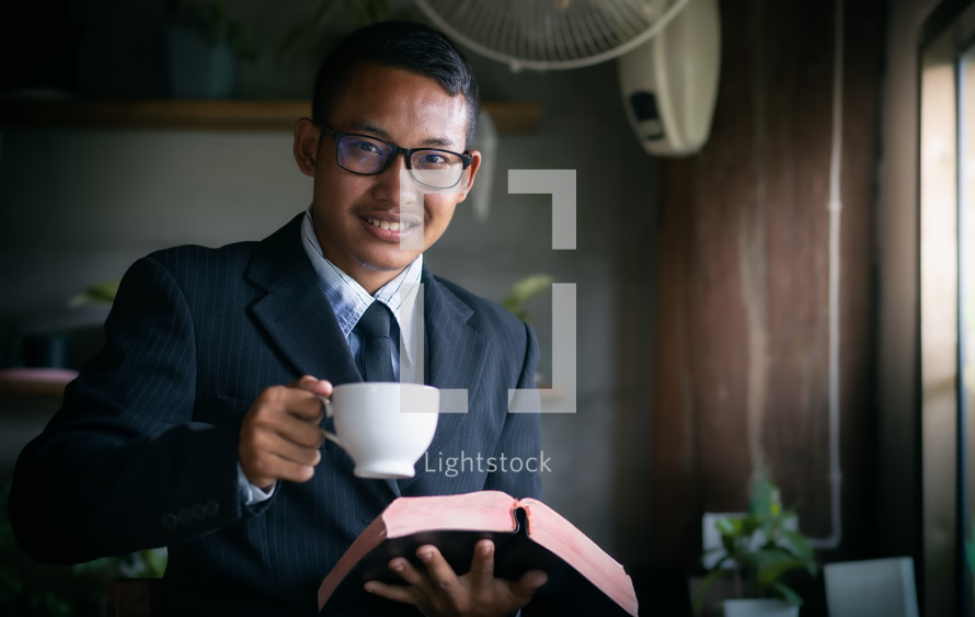 a man holding a coffee cup and a Bible 