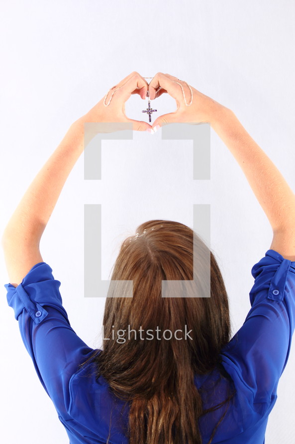 young woman holding up a cross and making a heart with her hands