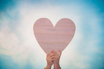 a child's hand holding up a wooden heart 