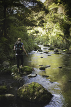 woman backpacking across moss covered rocks in a stream 