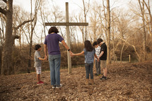 holding hands in prayer around a cross 