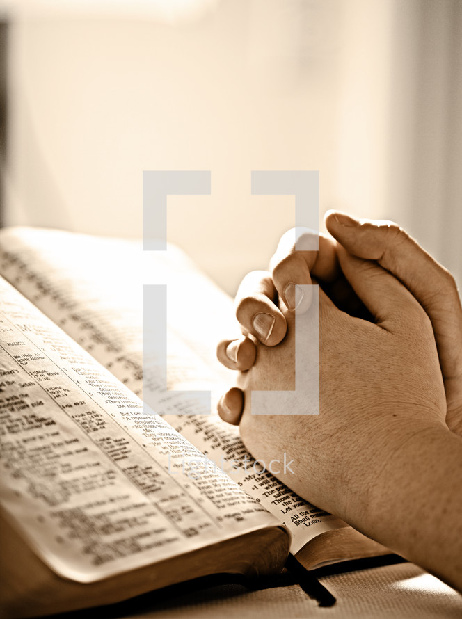 Prayer hands on top of open Bible.
