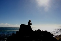 silhouette of a man crouched on a sea cliff