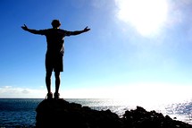 silhouette of a man with his arms outstretched on a sea cliff