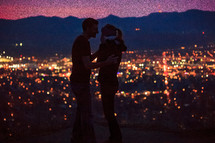 A couple in love in front of the lights from the suburbs below at night. 