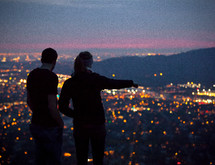 A couple standing and looking out at the lights from a suburb below