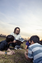 a young man reading a Bible to a group of children 