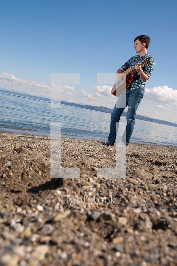 man playing a guitar in front of a lake