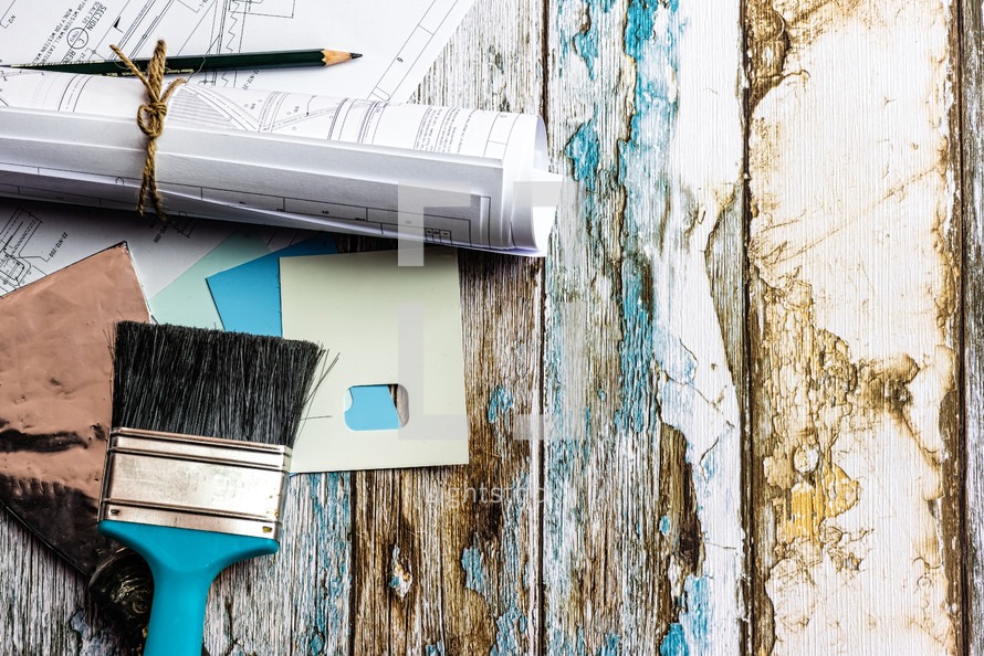 blueprints, paint brush, paint chips, pencil, and weathered wood background 