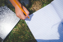 boy writing in a notebook in the grass