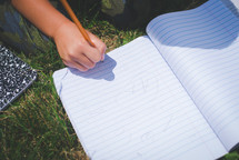 boy writing in a notebook on the grass
