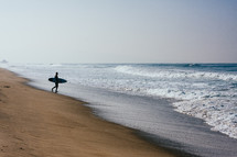 man with a surfboard walking on a beach 