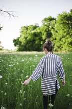 a woman walking through a field of wildflowers 