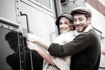 Young couple dressed in 1940's clothing, standing on the steps leading into an old train,