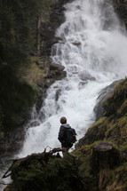 man hiking up a mountain near a waterfall 
