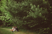 Teens sitting outside in the grass near trees.